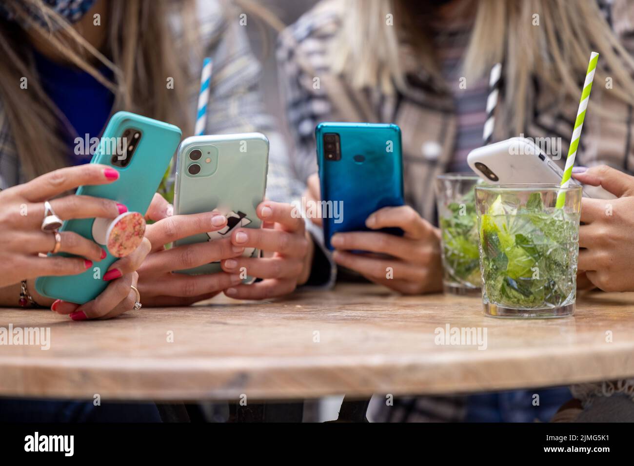 Gros plan des mains d'un groupe multiracial de quatre femmes utilisant un smartphone à la table dans un café de la ville avec des cocktails et dri Banque D'Images