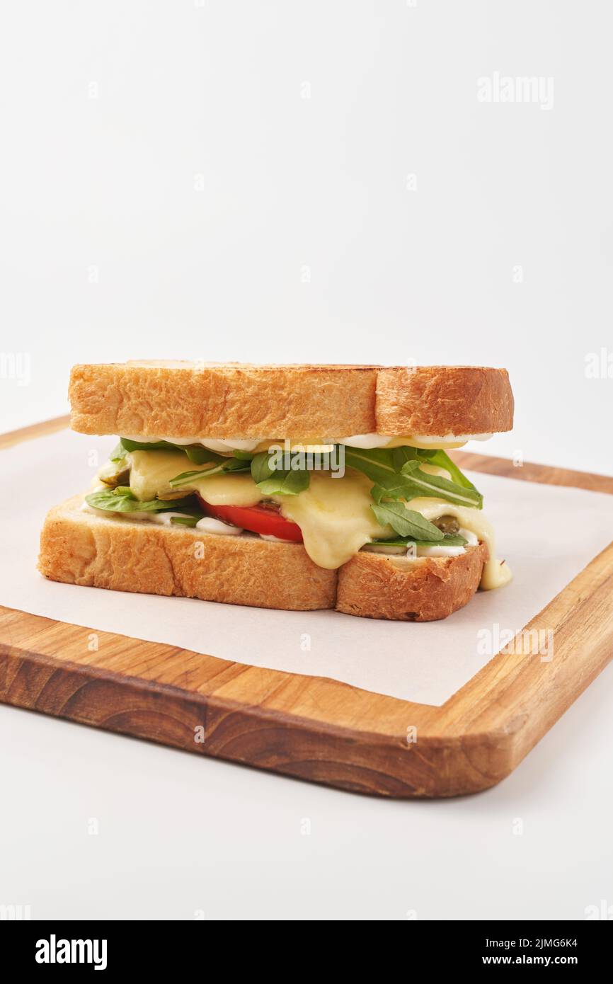 Délicieux pain doré grillé de sandwich farci de feuilles d'arugula vertes et de légumes avec du fromage fondu et servi sur une planche de bois avec du papier Banque D'Images