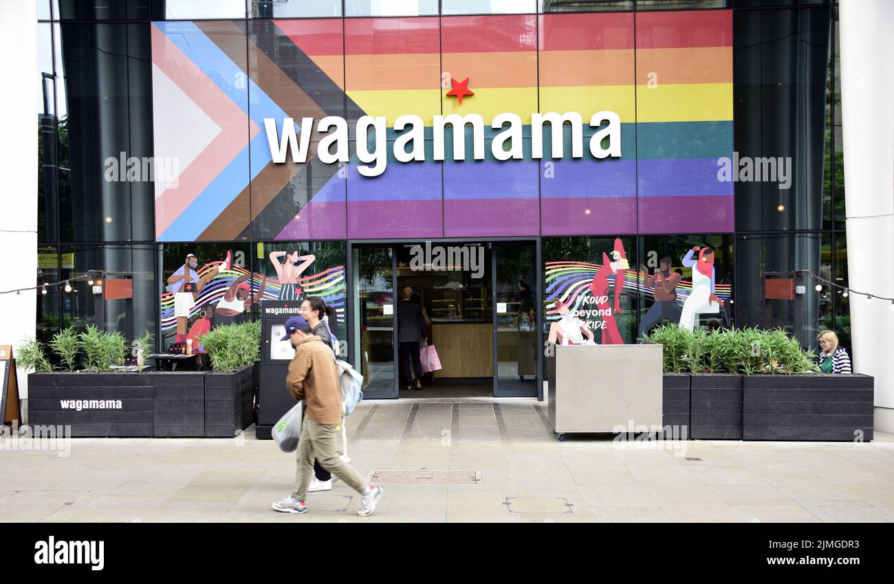Les gens passent devant le restaurant Wagamama, la place Saint-Pierre, Manchester, Royaume-Uni, maintenant avec le drapeau de progrès sur sa façade. Banque D'Images