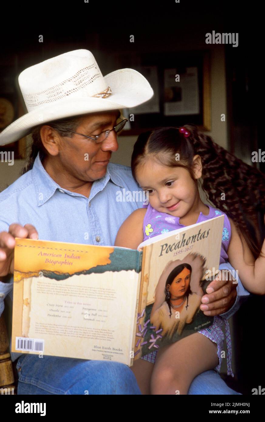 Famille amérindienne d'un grand-père lisant un livre d'histoire sur Pocahontas à sa jeune petite-fille. Banque D'Images