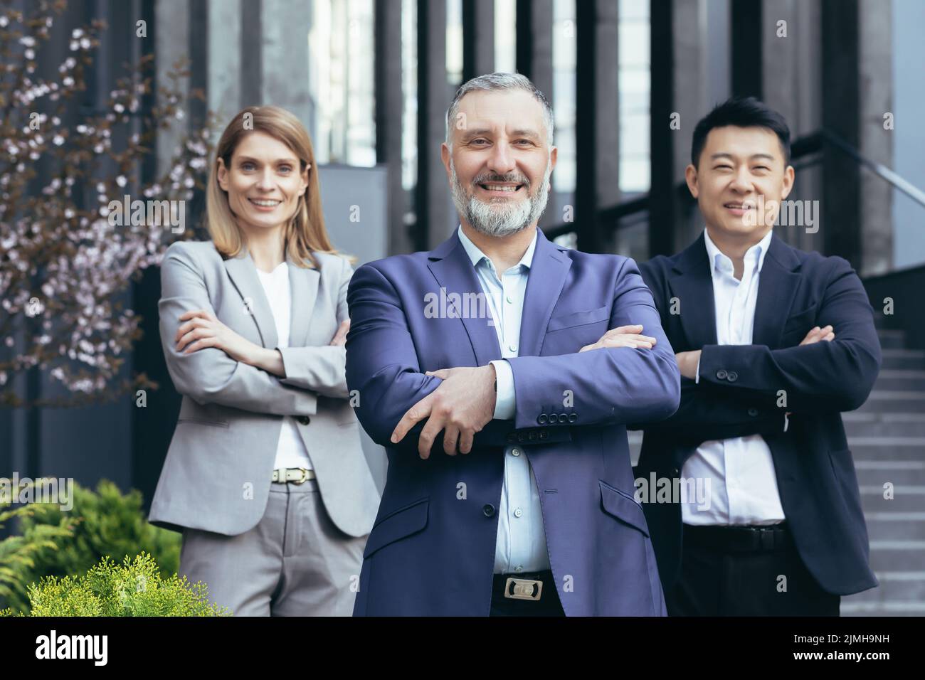 équipe de rêve diversifiée, patron d'homme d'affaires à cheveux gris senior avec des collègues à l'extérieur du bureau souriant et regardant la caméra avec les bras croisés Banque D'Images