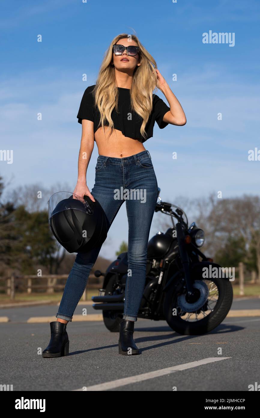 Un beau modèle Blonde apprécie le temps en extérieur en posant avec sa moto Banque D'Images