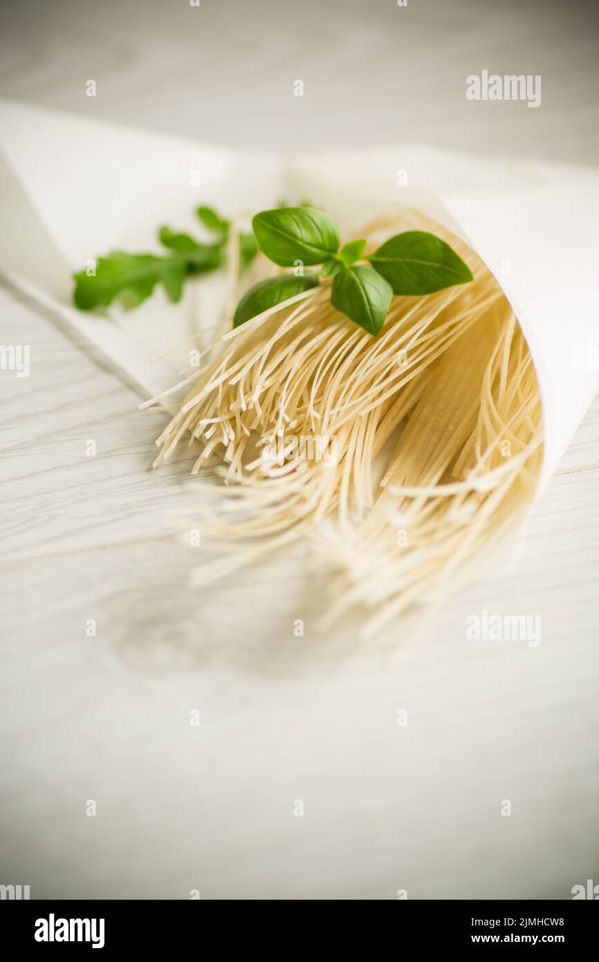 nouilles aux œufs séchées faites maison dans un sac de papier au basilic, sur une table en bois Banque D'Images