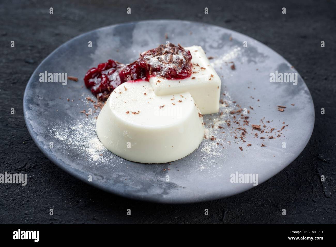 Le pudding traditionnel aux amandes de lancmange de style moderne, avec coulis de cerises acides et chapelure de chocolat, est servi en gros plan dans une pièce design Banque D'Images