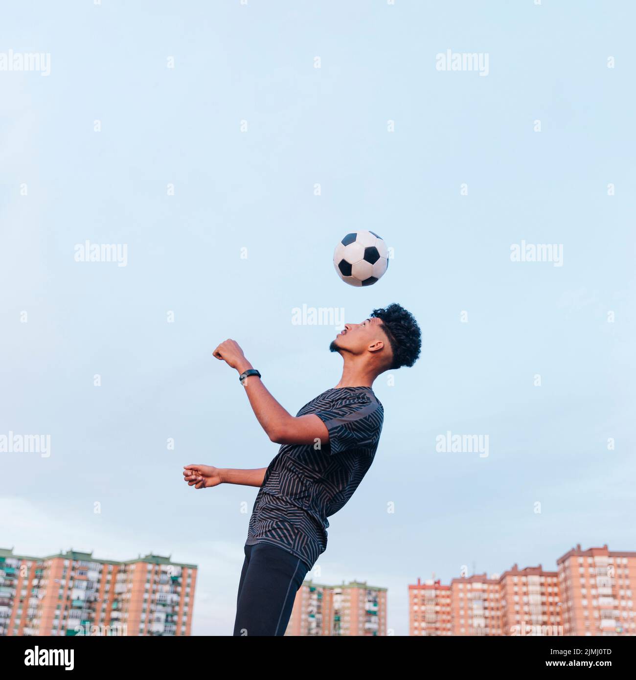 Entraînement d'athlète masculin avec ballon de football contre ciel bleu Banque D'Images