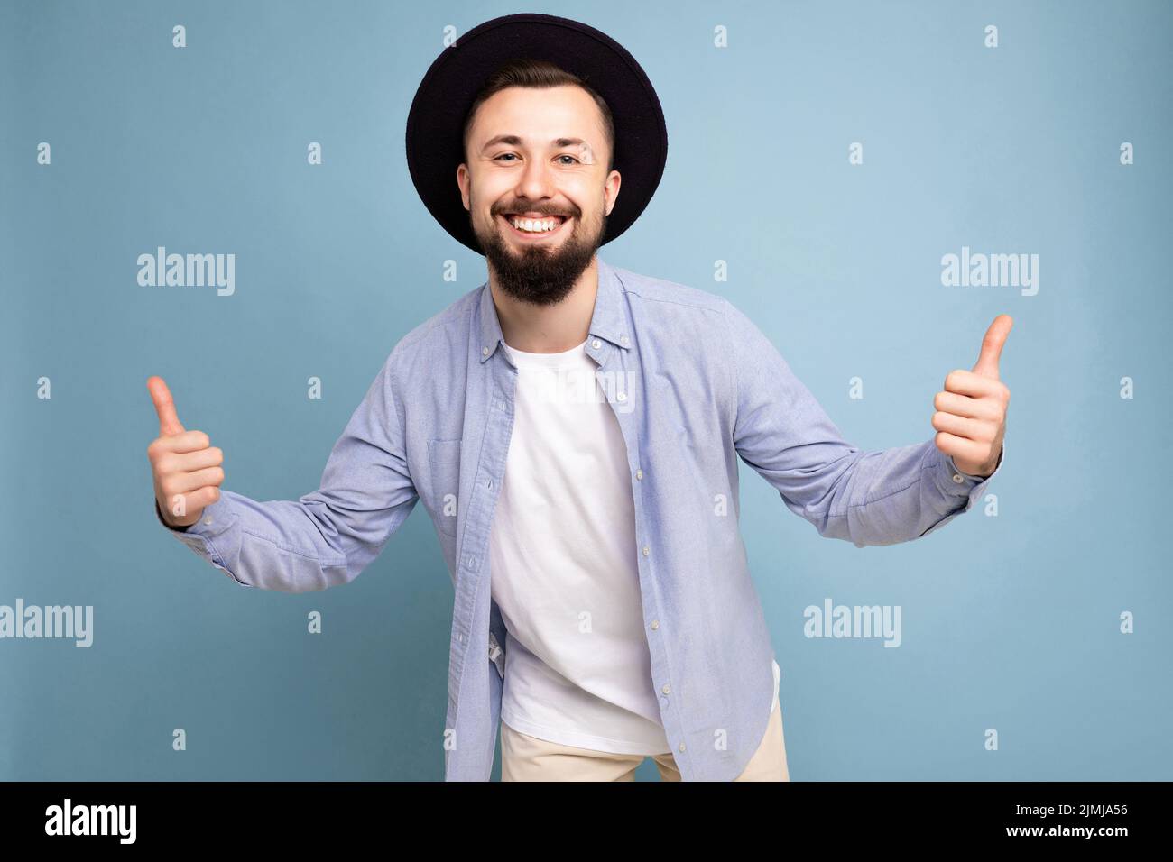 Photo de positif heureux souriant bon look jeune brunet barbu homme portant une chemise bleue décontractée et un t-shirt blanc et styli Banque D'Images