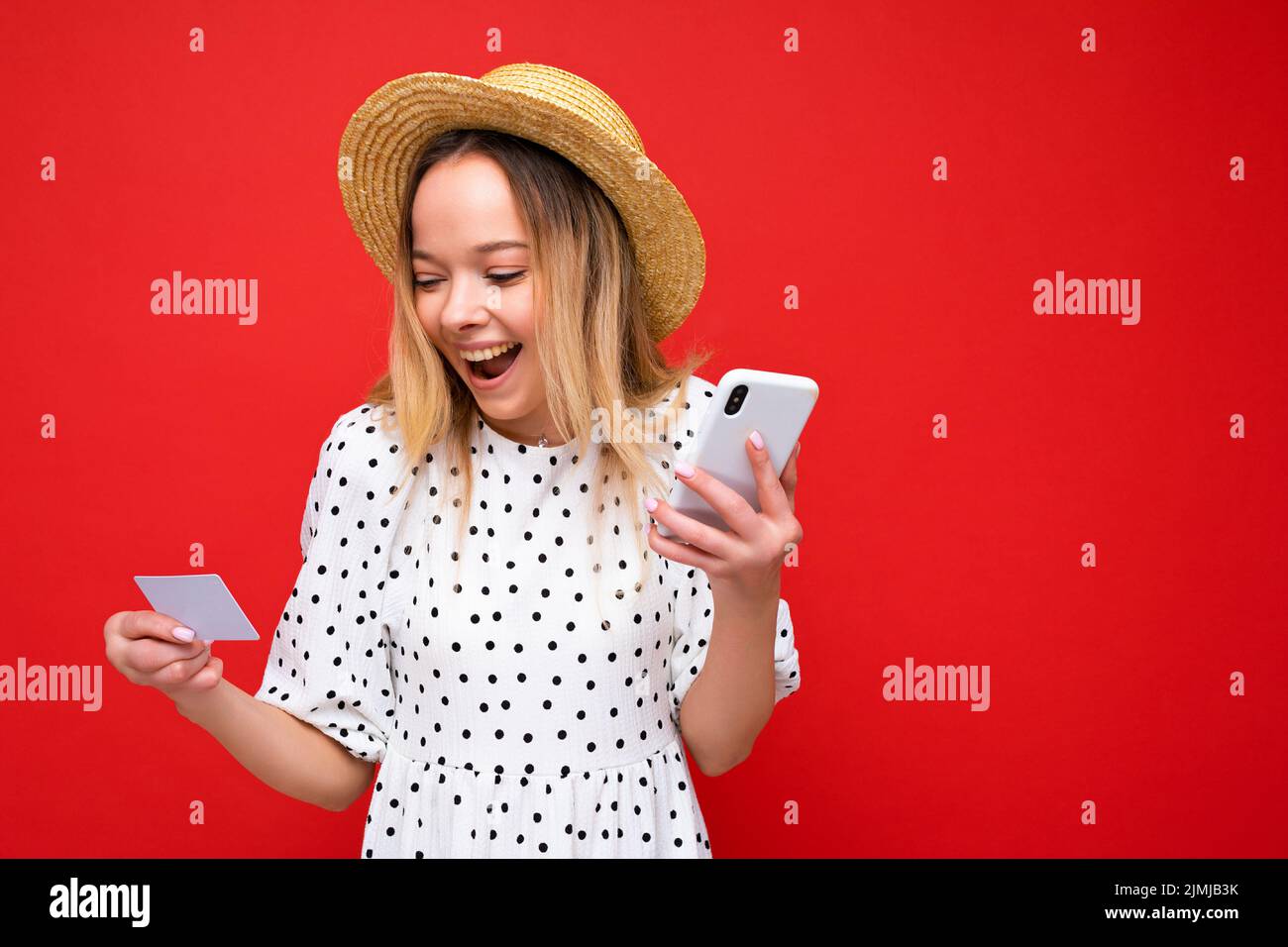Photo de la belle positive surprise jeune blonde femme dans les vêtements d'été en utilisant le téléphone cellulaire et tenant la carte de crédit faisant payer Banque D'Images