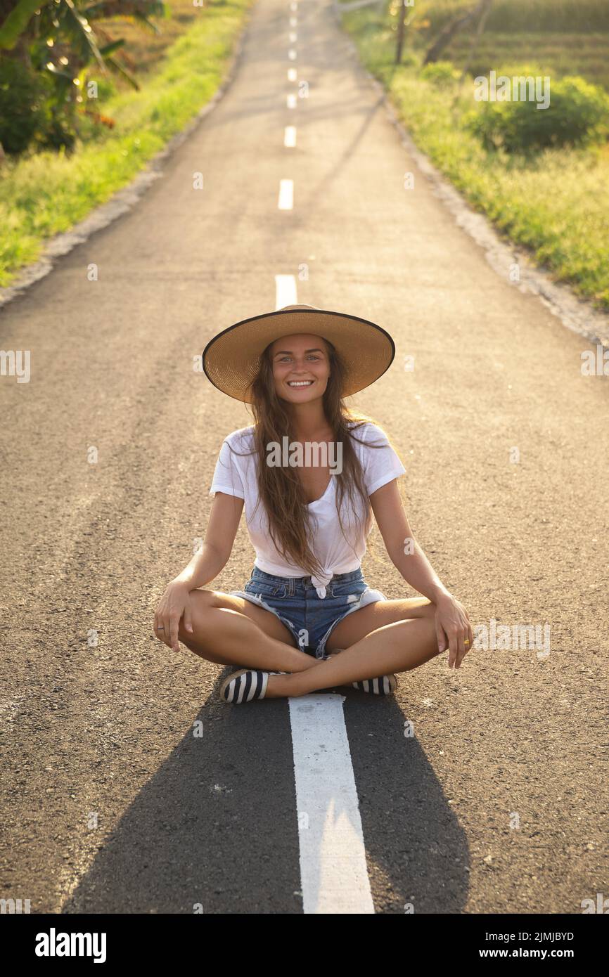 Une femme heureuse est assise au milieu de la route asphaltée Banque D'Images