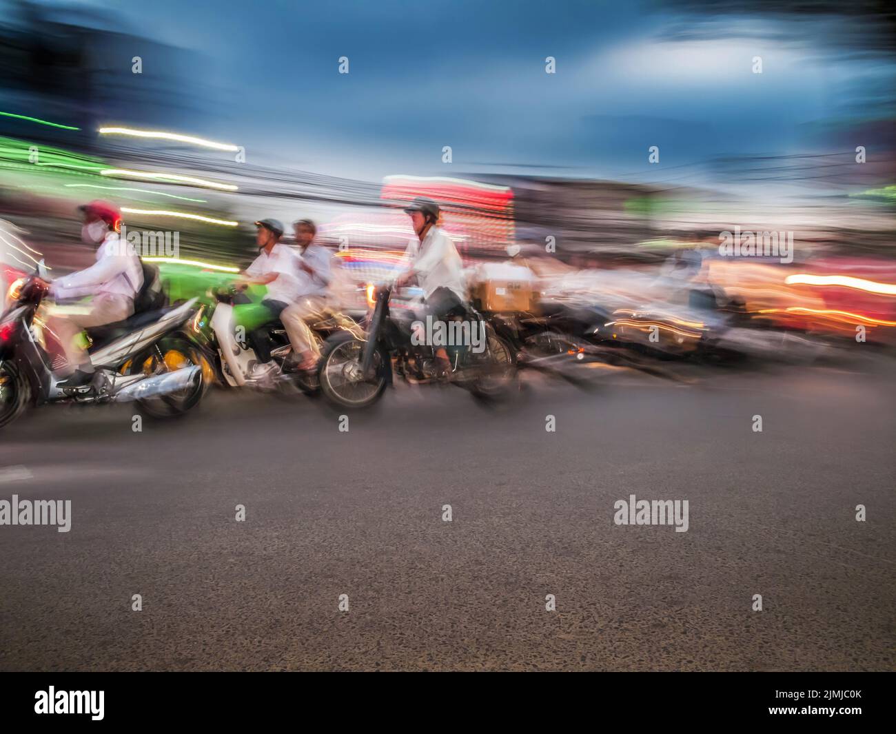 Les motocyclistes circulent dynamiquement le long d'une rue urbaine éclairée pendant le crépuscule Banque D'Images