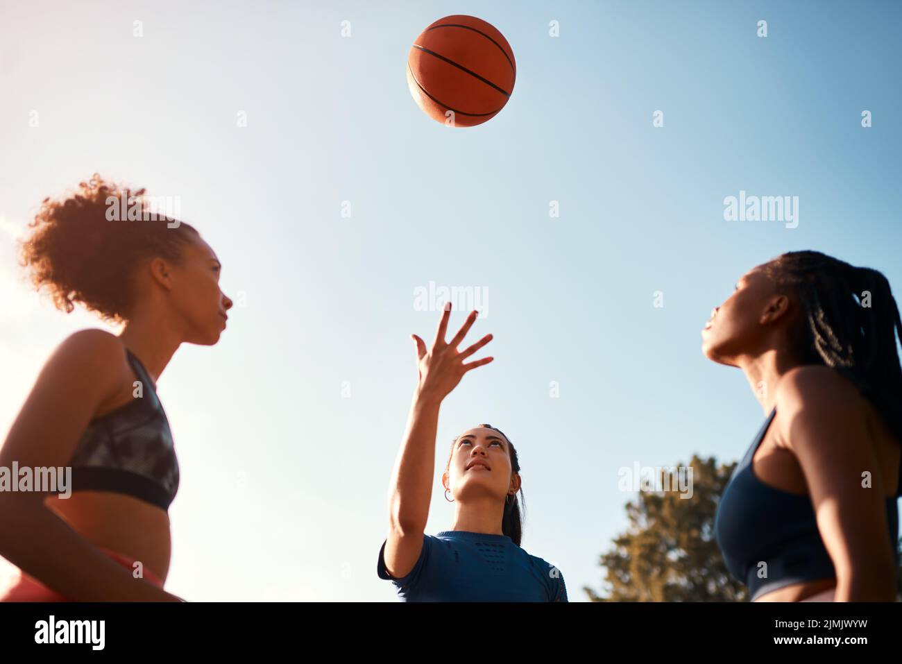 Le premier à obtenir le ballon commence. Un groupe diversifié de sportswomen jouant un jeu de basket-ball de compétition ensemble pendant la journée. Banque D'Images