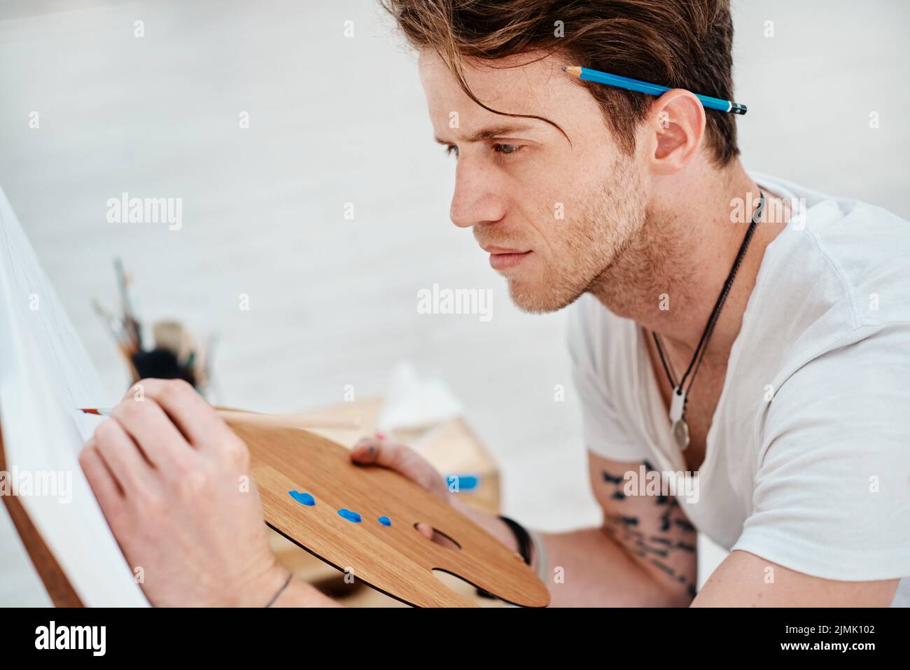 L'art est un chemin vers la découverte de soi. Un beau jeune artiste assis et regardant contemplatif pendant un cours d'art dans le studio. Banque D'Images