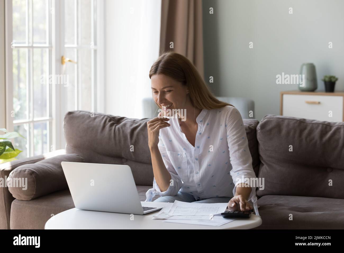 Une femme s'assoit à table avec un ordinateur portable compte les revenus semblent satisfaits Banque D'Images