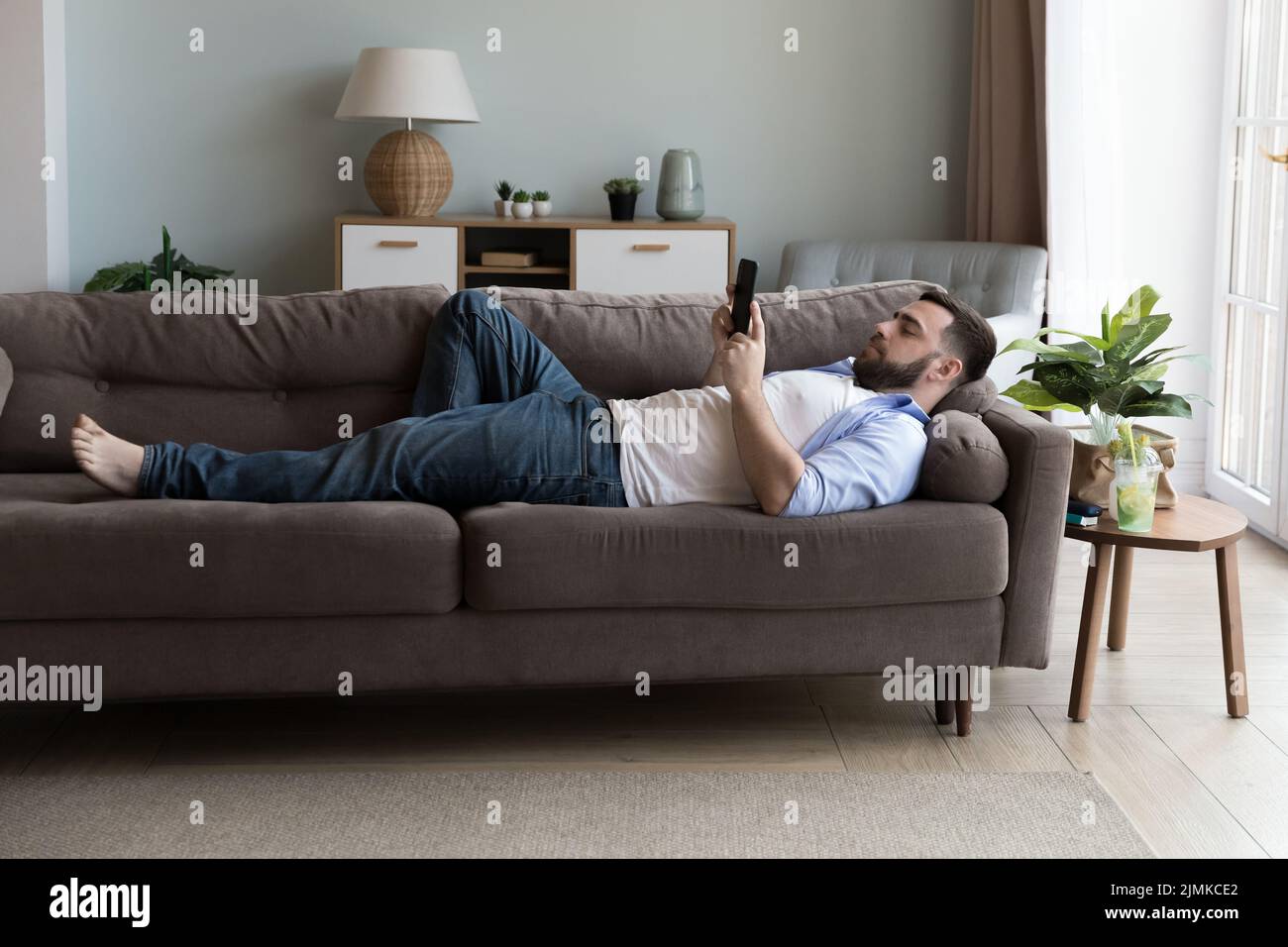 L'homme utilise un smartphone moderne allongé sur un canapé dans le salon Banque D'Images