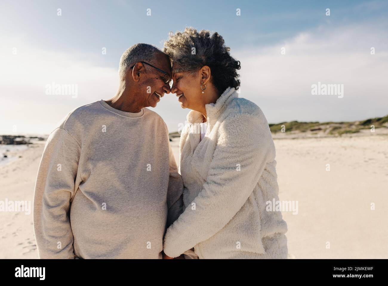 Couple de personnes âgées souriant et se touchant la tête ensemble à la plage. Couple senior joyeux partageant un moment romantique à l'extérieur. Couple heureux Banque D'Images