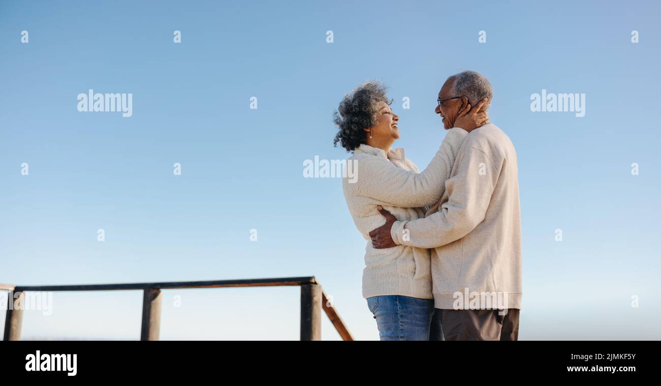 Heureux couple senior souriant les uns les autres en se tenant sur une promenade à la plage. Couple romantique de personnes âgées appréciant passer du temps de qualité ensemble Banque D'Images