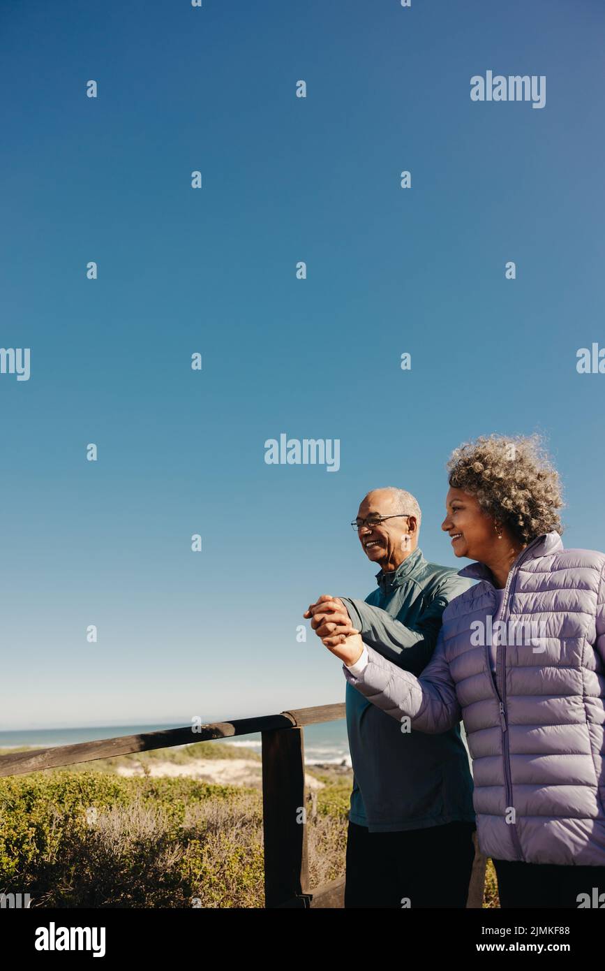 Promenade romantique le long de la plage. Un couple âgé à la retraite souriant et tenant les mains tout en marchant ensemble le long d'une promenade. Joyeux couple de personnes âgées enjoyi Banque D'Images