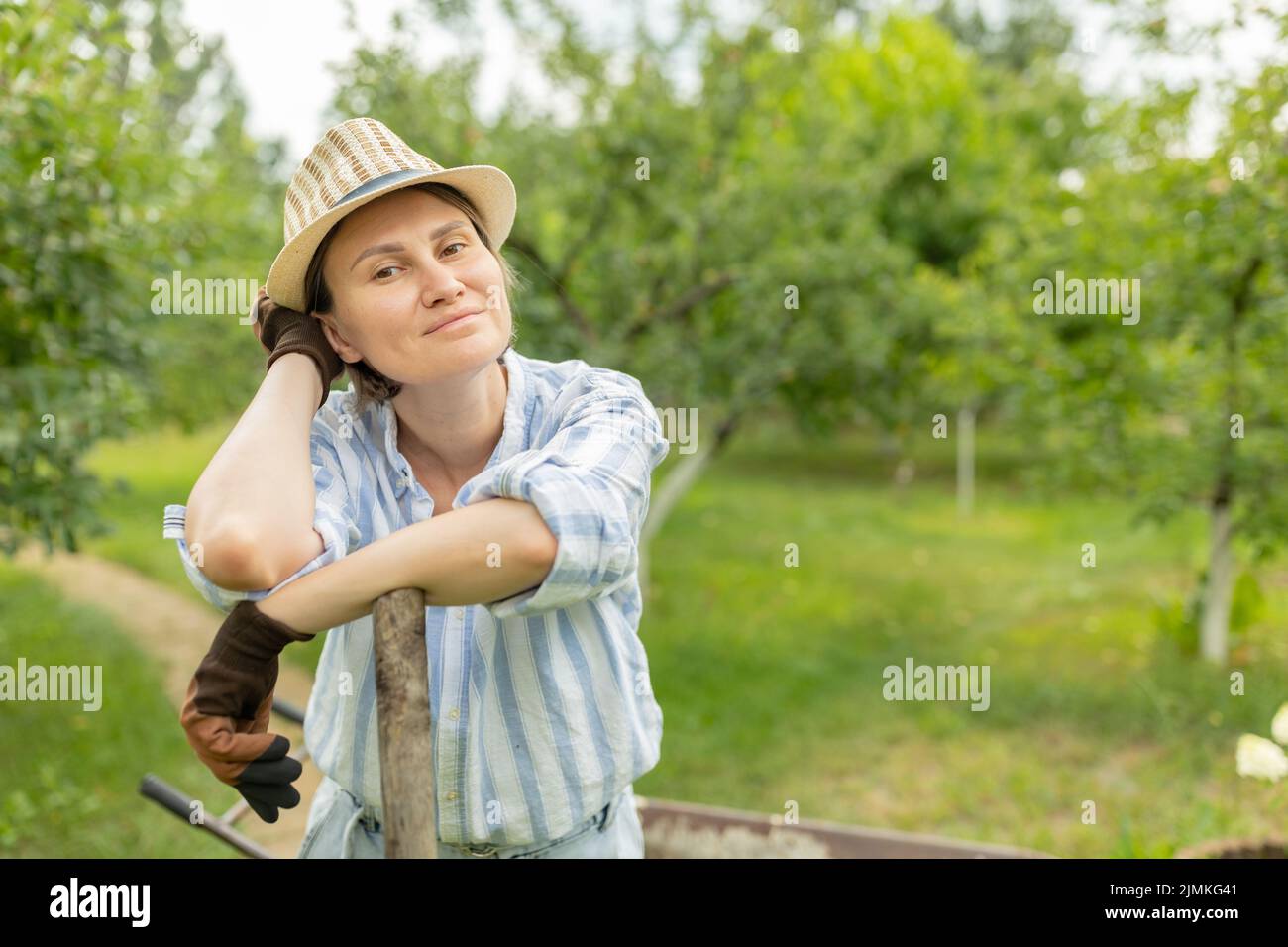 paysan femme se reposant de dur labeur par la brouette pleine de fumier animal sur les terres agricoles ou le jardin Banque D'Images
