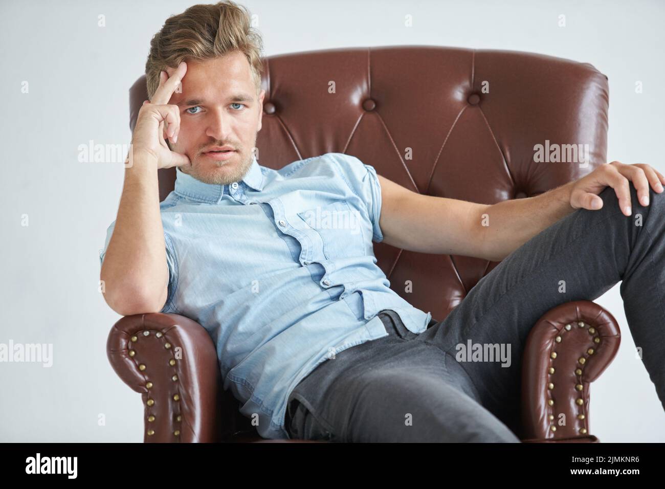 Portrait d'un homme intelligent, élégant, charismatique, non rasé petite chemise bleue, assis sur un fauteuil en cuir brun, dialogue, négociations Banque D'Images