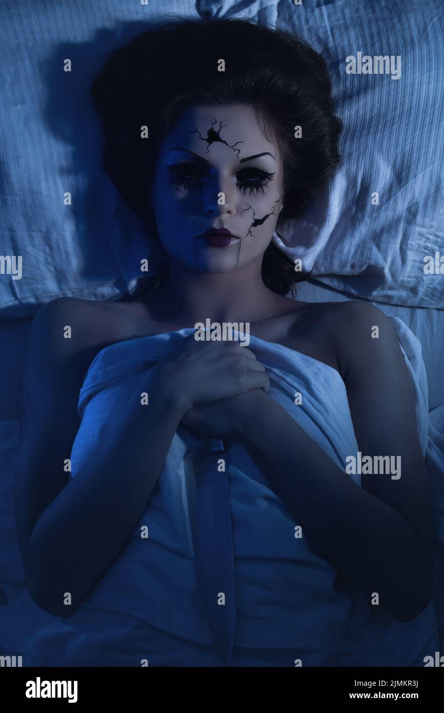 Poupée parlante en porcelaine tenant le couteau et allongé dans le lit Banque D'Images