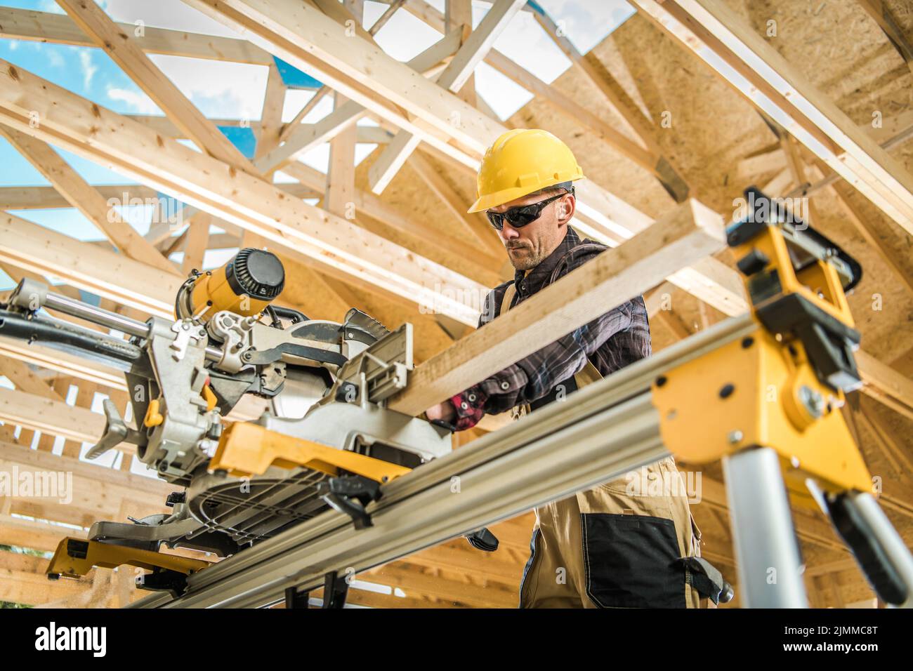 Travailleur de la construction en casque dur jaune coupant une planche ...