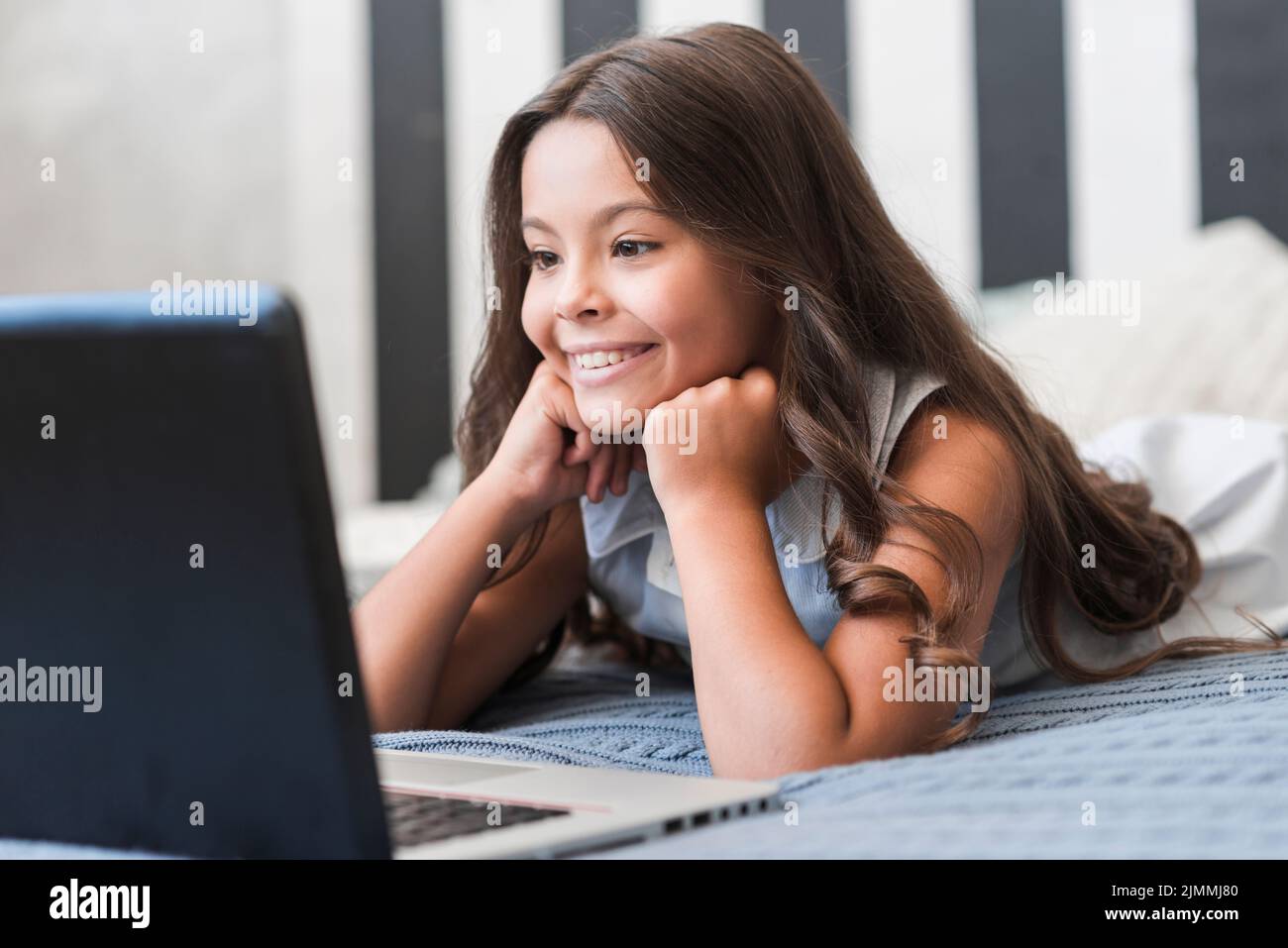 Jolie fille souriante couchée lit regarder un ordinateur portable vidéo Banque D'Images