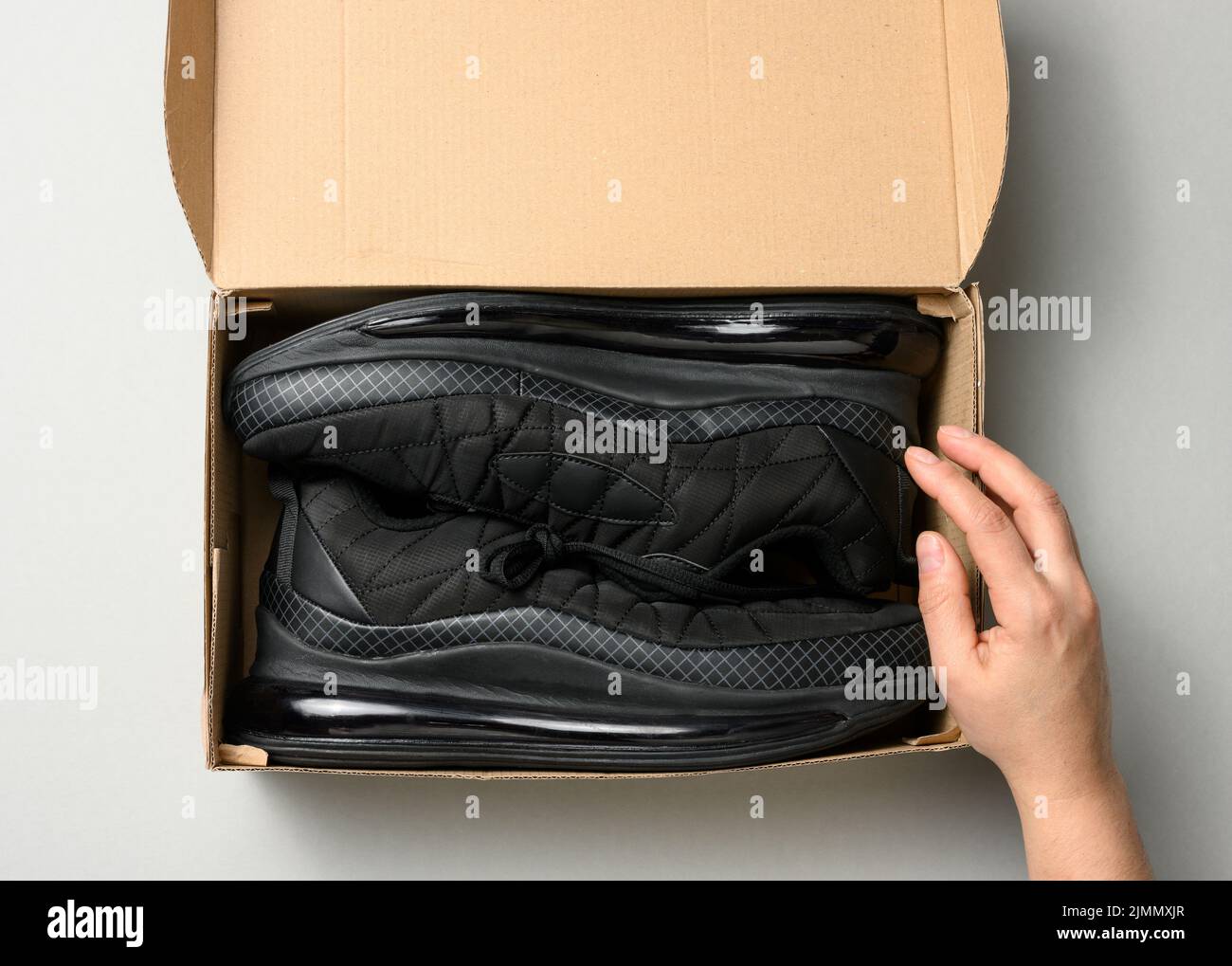 Les femmes tiennent une boîte en carton marron avec des baskets de sport noires sur une table grise, inspectant une commande en ligne, vue du dessus Banque D'Images