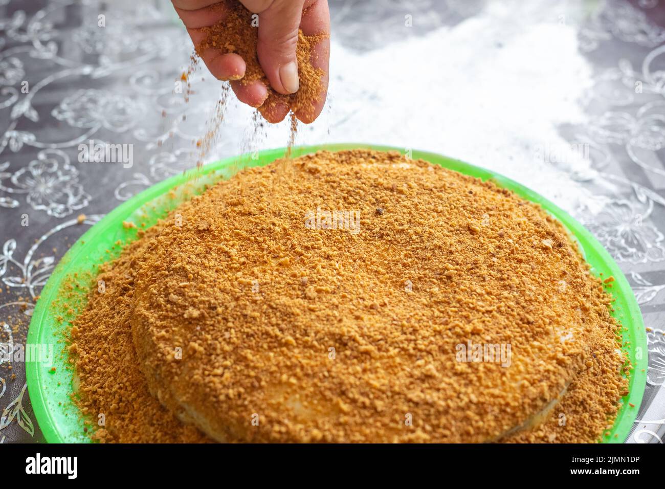 Cuisson de gâteaux faits maison. Une femme saupoudrer un gâteau cuit et couvert de crème avec de la chapelure de confiserie. Banque D'Images