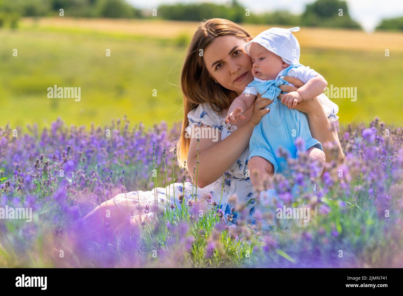 Adorable petit garçon dans un costume bleu étant tenu par sa mère aimante se détendant parmi les fleurs de lavande pourpres Banque D'Images