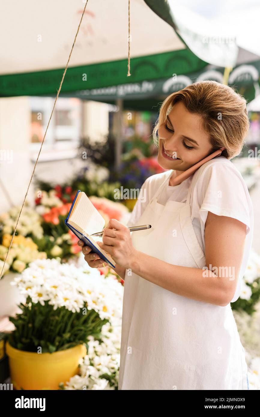 Belle femme fleuriste prenant l'ordre par téléphone dans sa petite boutique de fleurs Banque D'Images