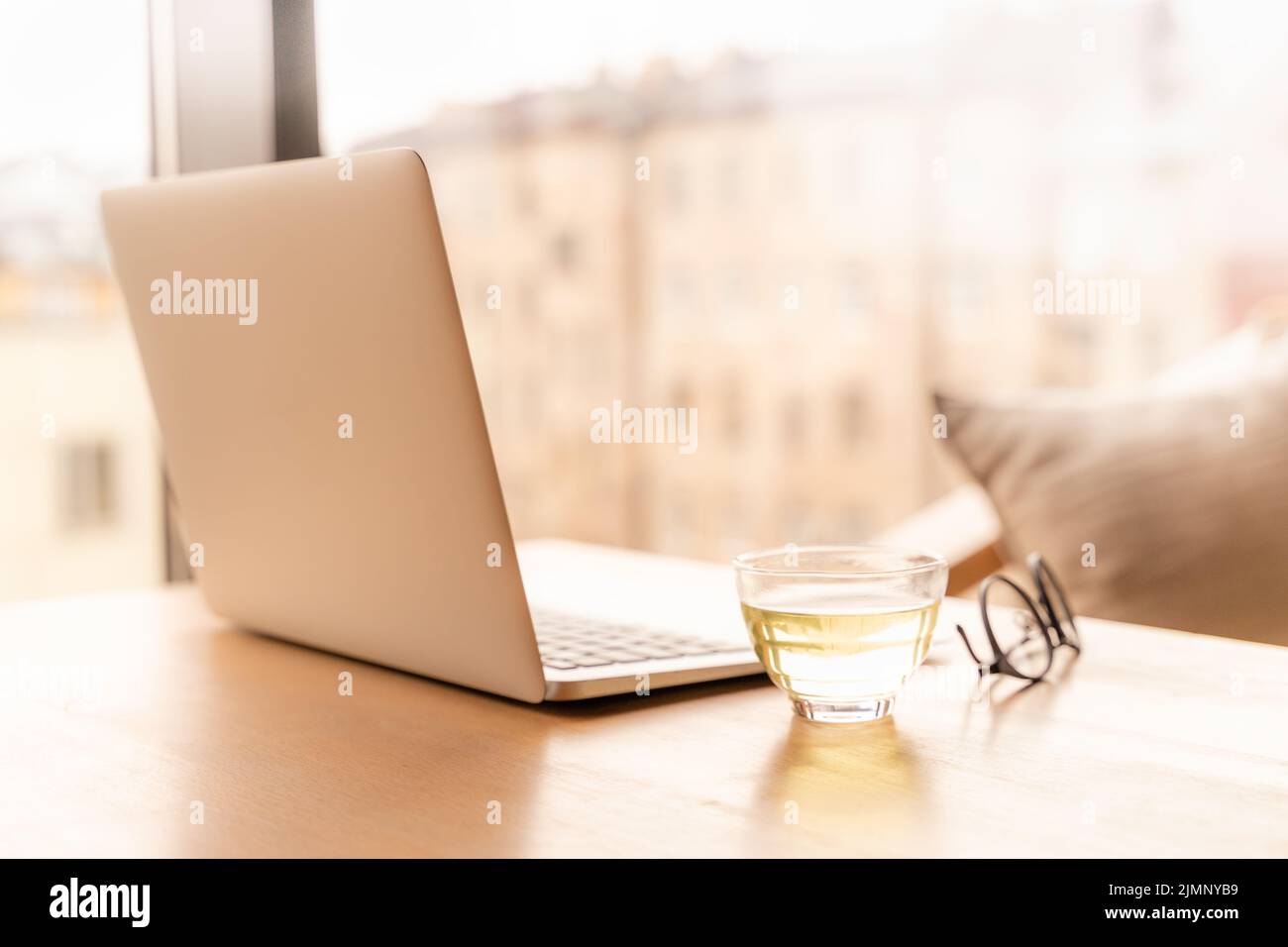 Bureau indépendant avec ordinateur portable ouvert, tasse de thé vert et verres sur table. Banque D'Images