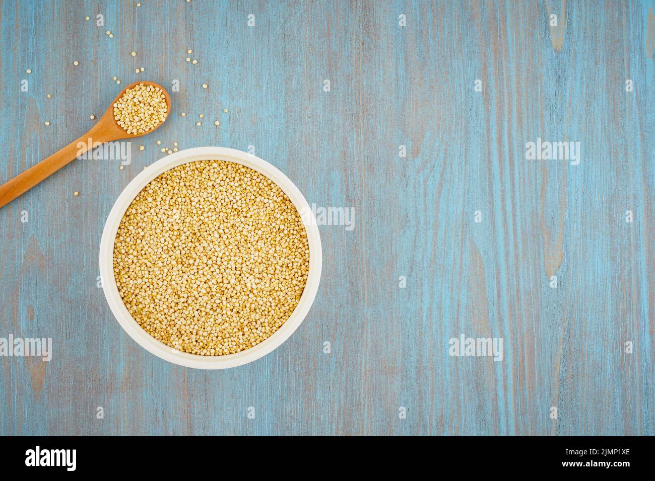 Grain de quinoa dans un bol blanc et une cuillère sur une table bleue, copier l'espace Banque D'Images