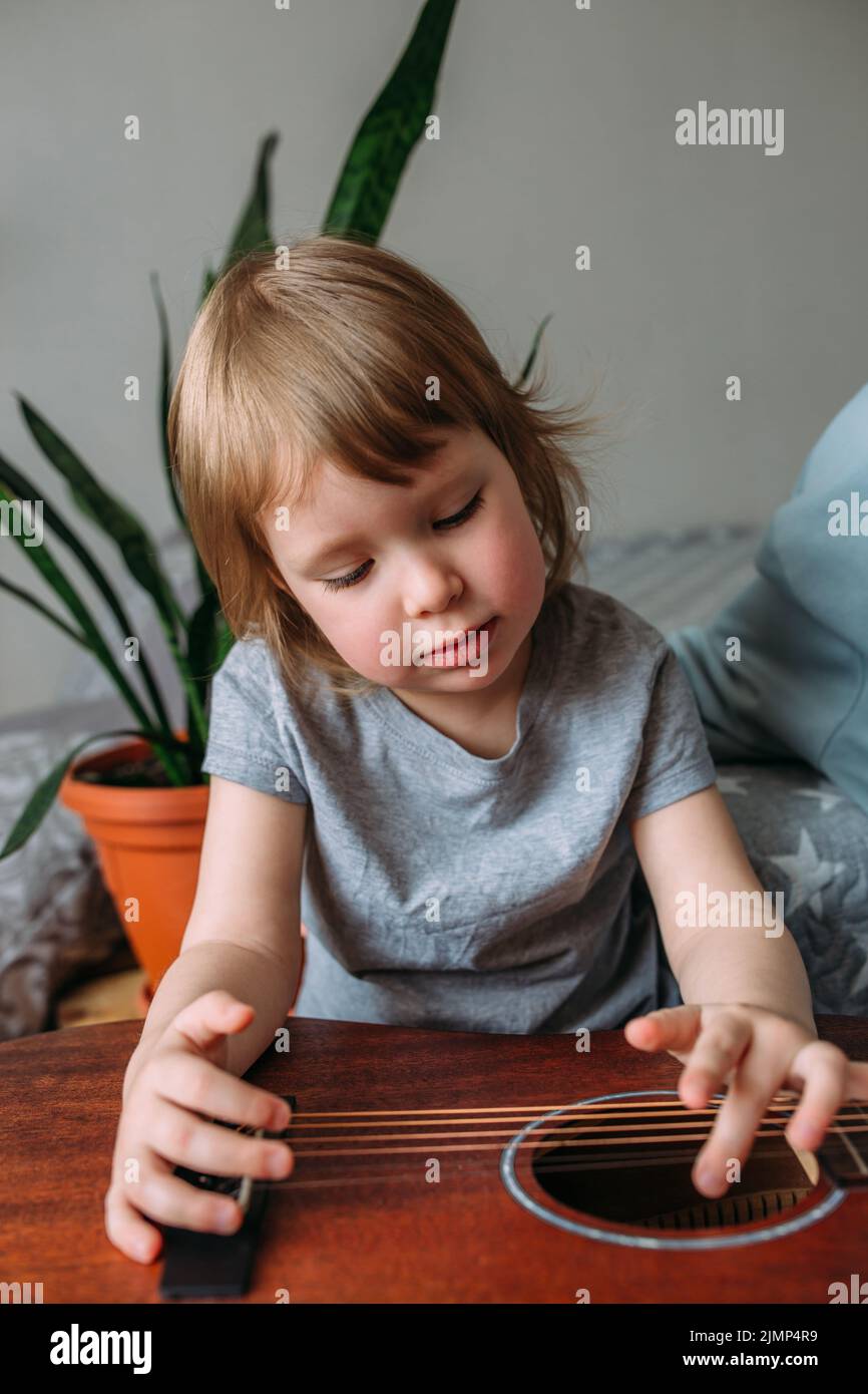 Un enfant mignon joue avec une grosse guitare acoustique à la maison Banque D'Images