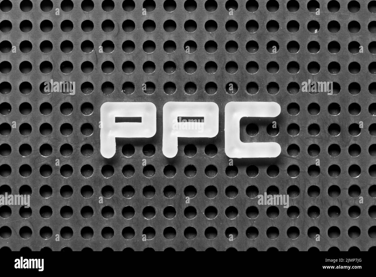 Lettre blanche en lettres de l'alphabet dans le mot PPC (abréviation de la rémunération par clic) sur fond noir du panneau perforé Banque D'Images