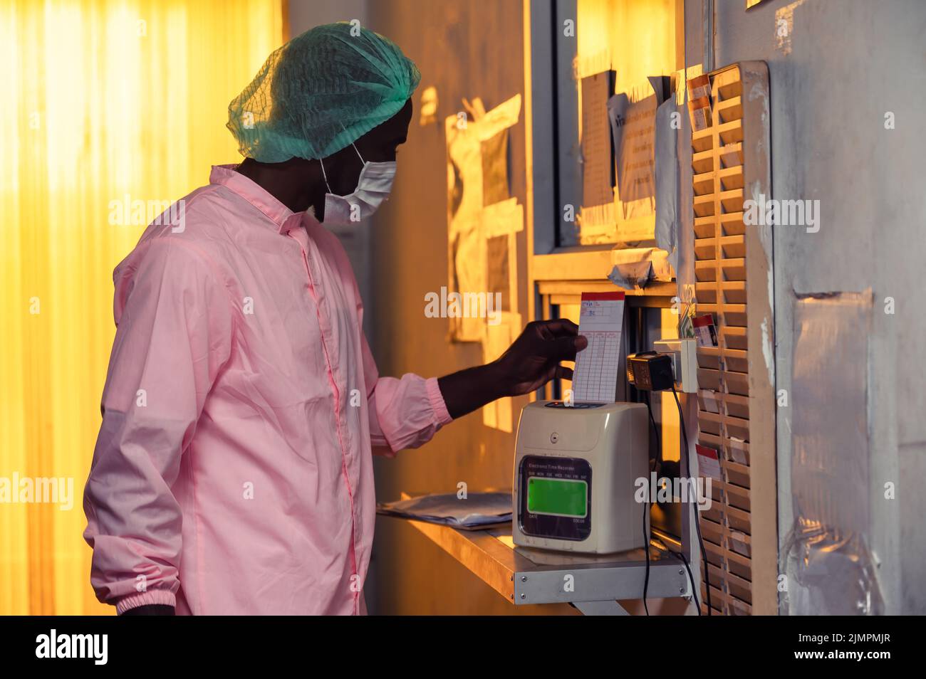 Un employé de contrôle de la qualité africain en costume stérile horloge avec le système d'horloge de la politique d'usine avant de travailler dans l'industrie de traitement d'entrepôt Banque D'Images