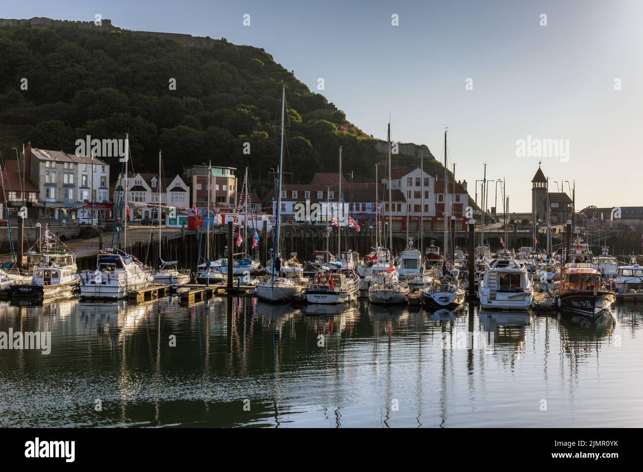 Tôt le matin, le soleil éclaire les bateaux et les yachts amarrés dans le port de Scarborough, avec le château de Scarborough en arrière-plan. Banque D'Images