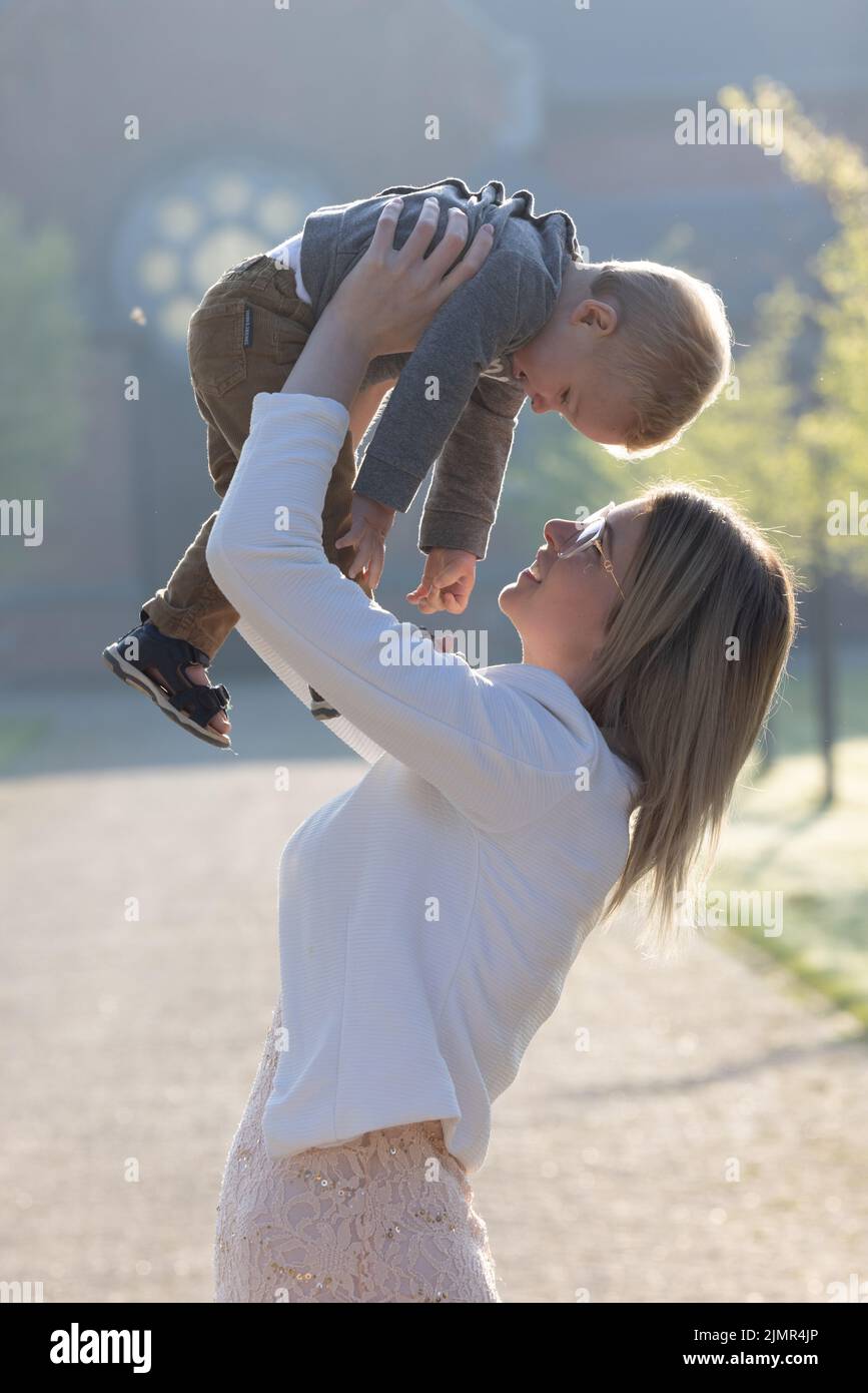Une jeune mère heureuse avec un petit enfant dans ses bras, le regardant avec adoration et amour, se tient au milieu d'un parc en t Banque D'Images