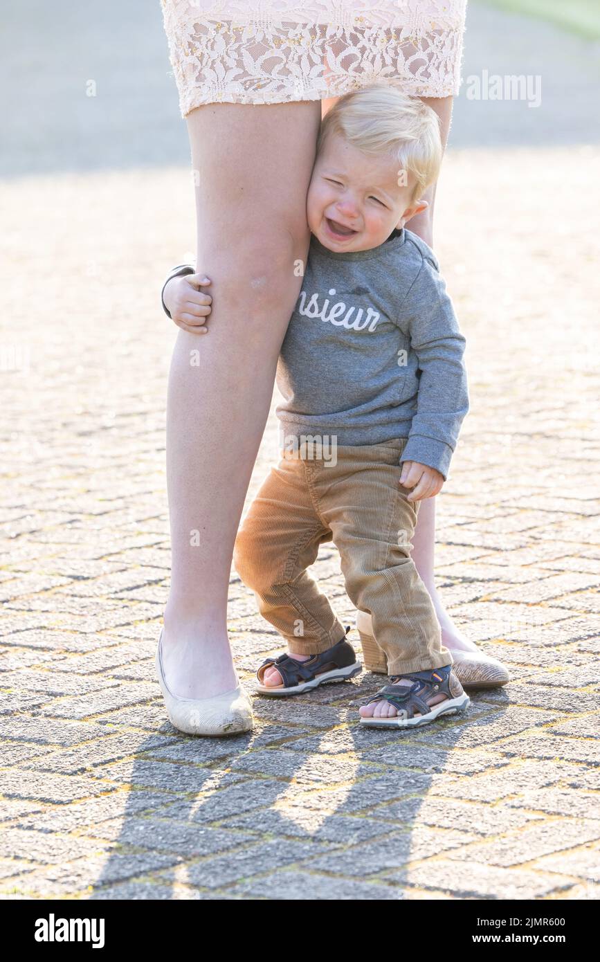 Triste casien blond petit garçon embrassant sa mère jambes Banque D'Images