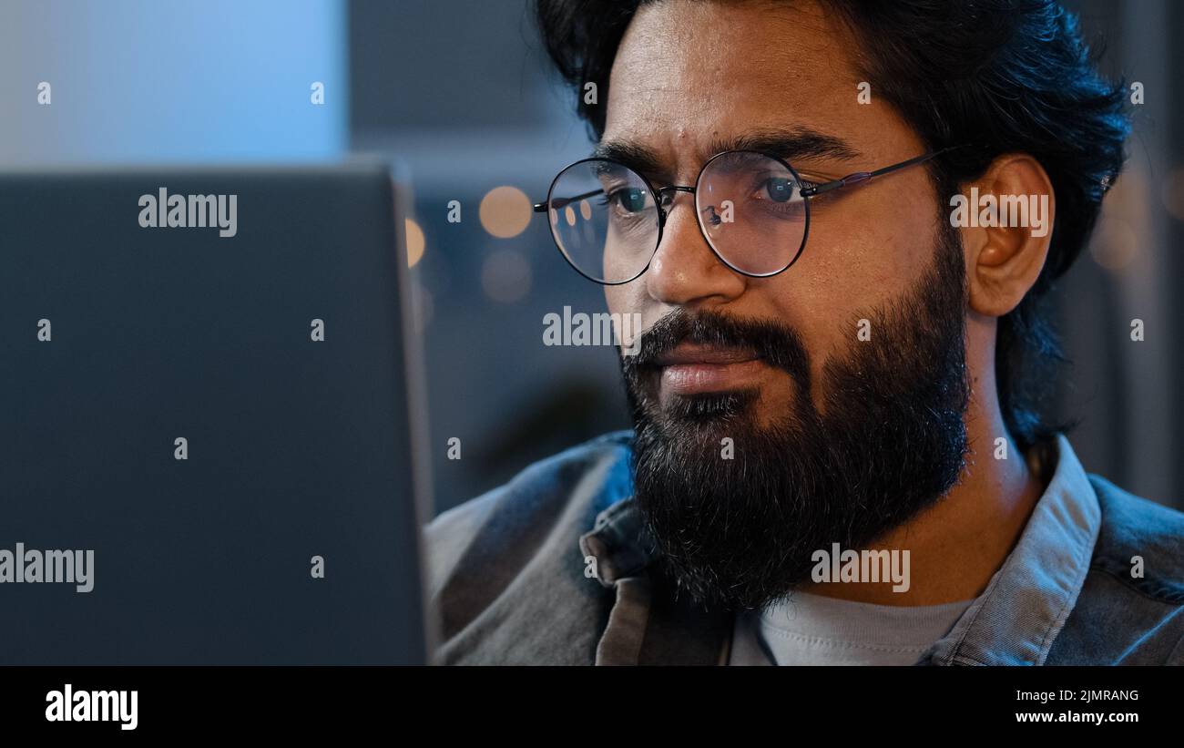 Gros plan sur un écran d'ordinateur portable, lumière à réflexion faciale mâle dans des lunettes. Un Indien arabe sérieux et concentré qui regarde l'informatique en freelance Banque D'Images