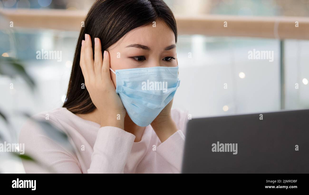 Confuse femme asiatique dans le masque médical lisant les mauvaises nouvelles sur la pandémie de covid19 recevoir refuser email sur ordinateur portable stress déprimé erreur désagréable en ligne Banque D'Images