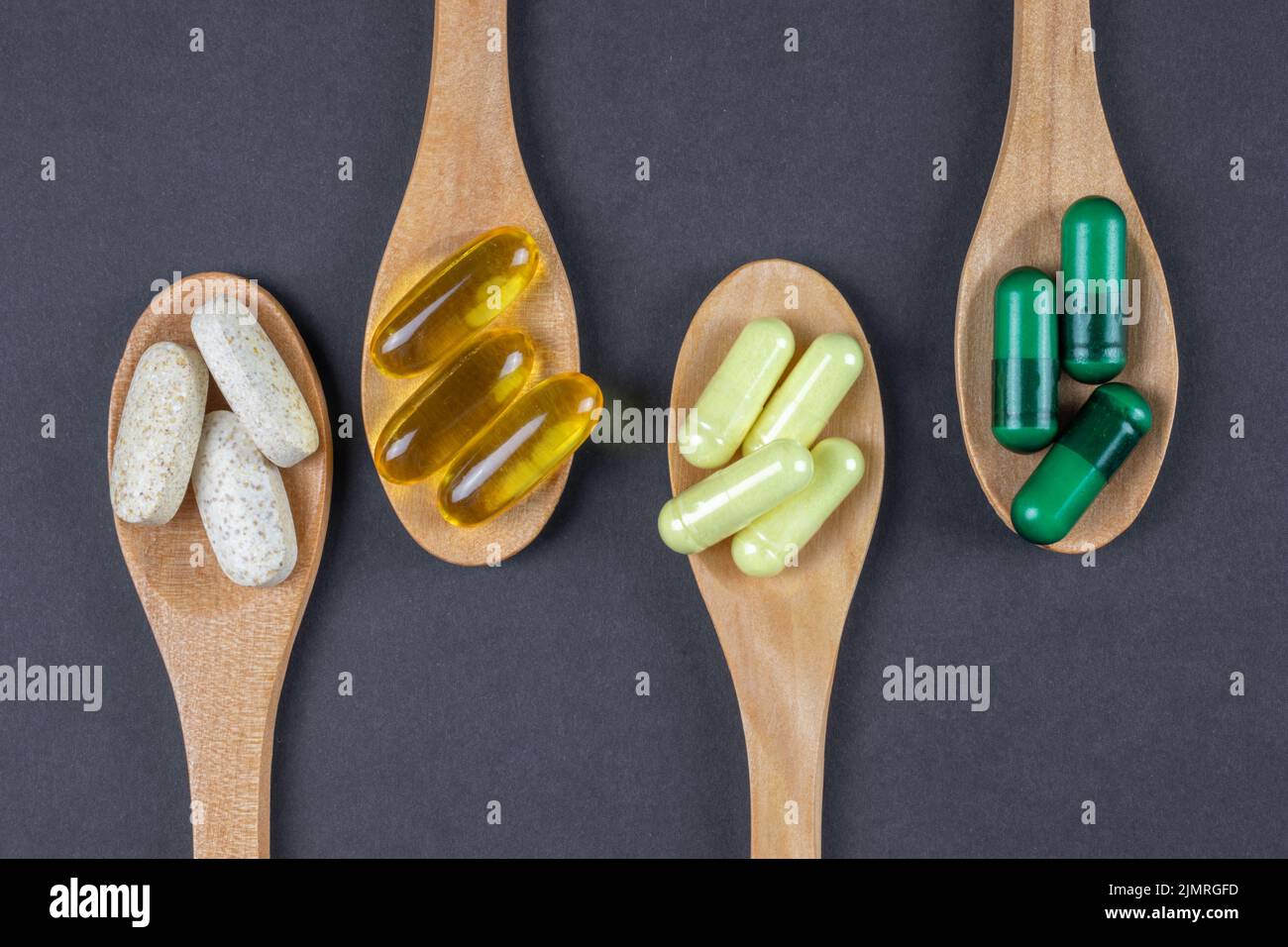 Petites cuillères en bois avec suppléments, vitamines et pilules en bois brun clair sur fond sombre, vue de dessus. Banque D'Images