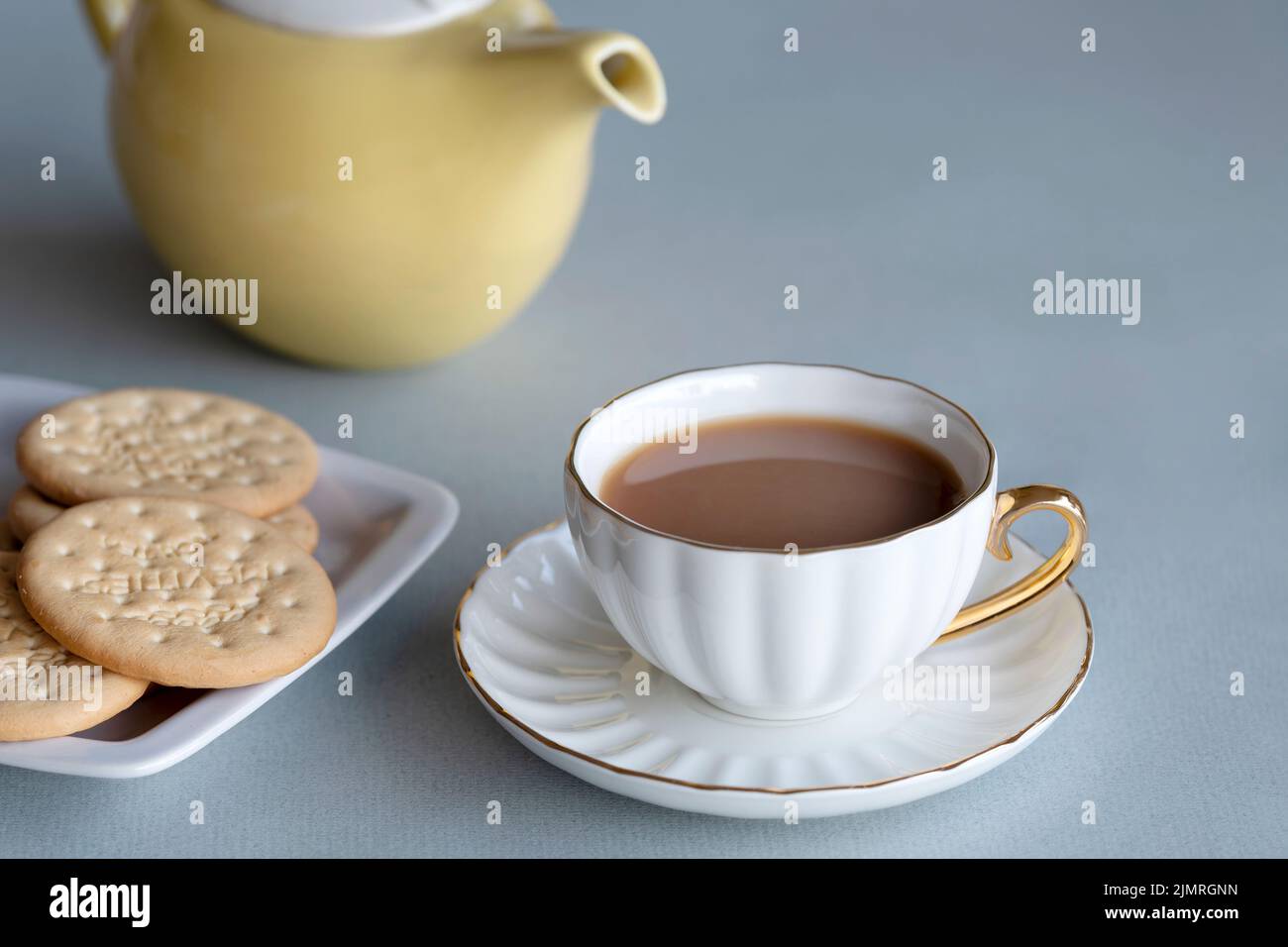 Une tasse de thé fraîchement brassée dans une tasse de porcelaine fine et soucoupe.le thé est servi avec deux biscuits de thé riche et la théière utilisée pour le faire est en vue Banque D'Images