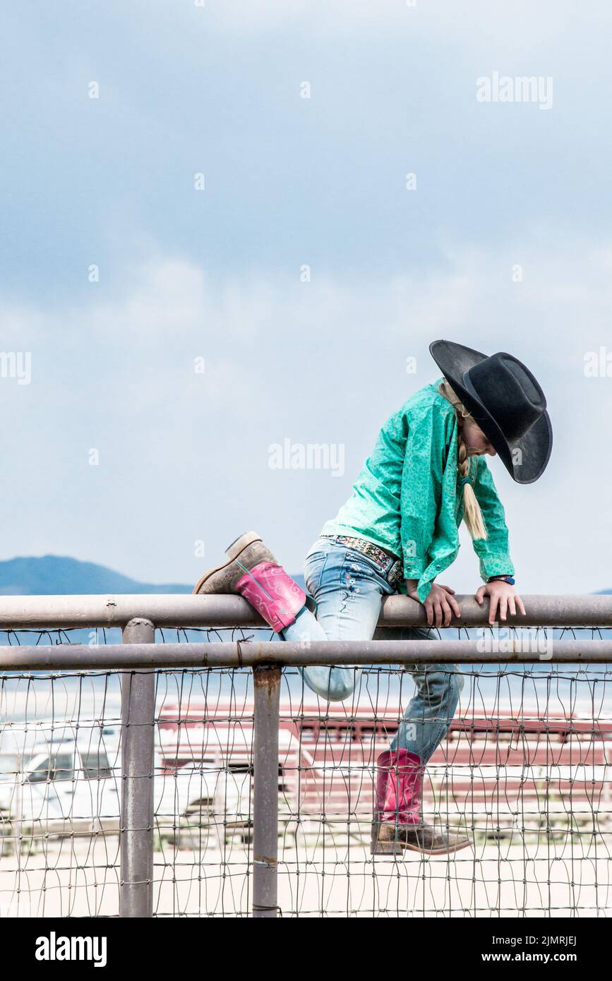 Une jeune cow-girl monte sur une clôture à un corral de rodéo, vertical Banque D'Images