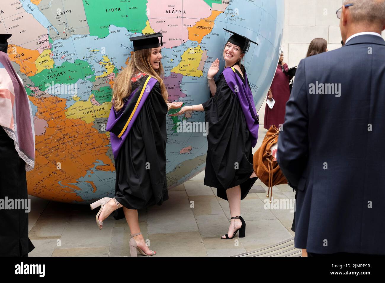 Les étudiants de la London School of Economics célèbrent l'obtention de leur diplôme à côté du monde retourné par l'artiste Mark Wallinger, lauréat du prix Turner. Banque D'Images