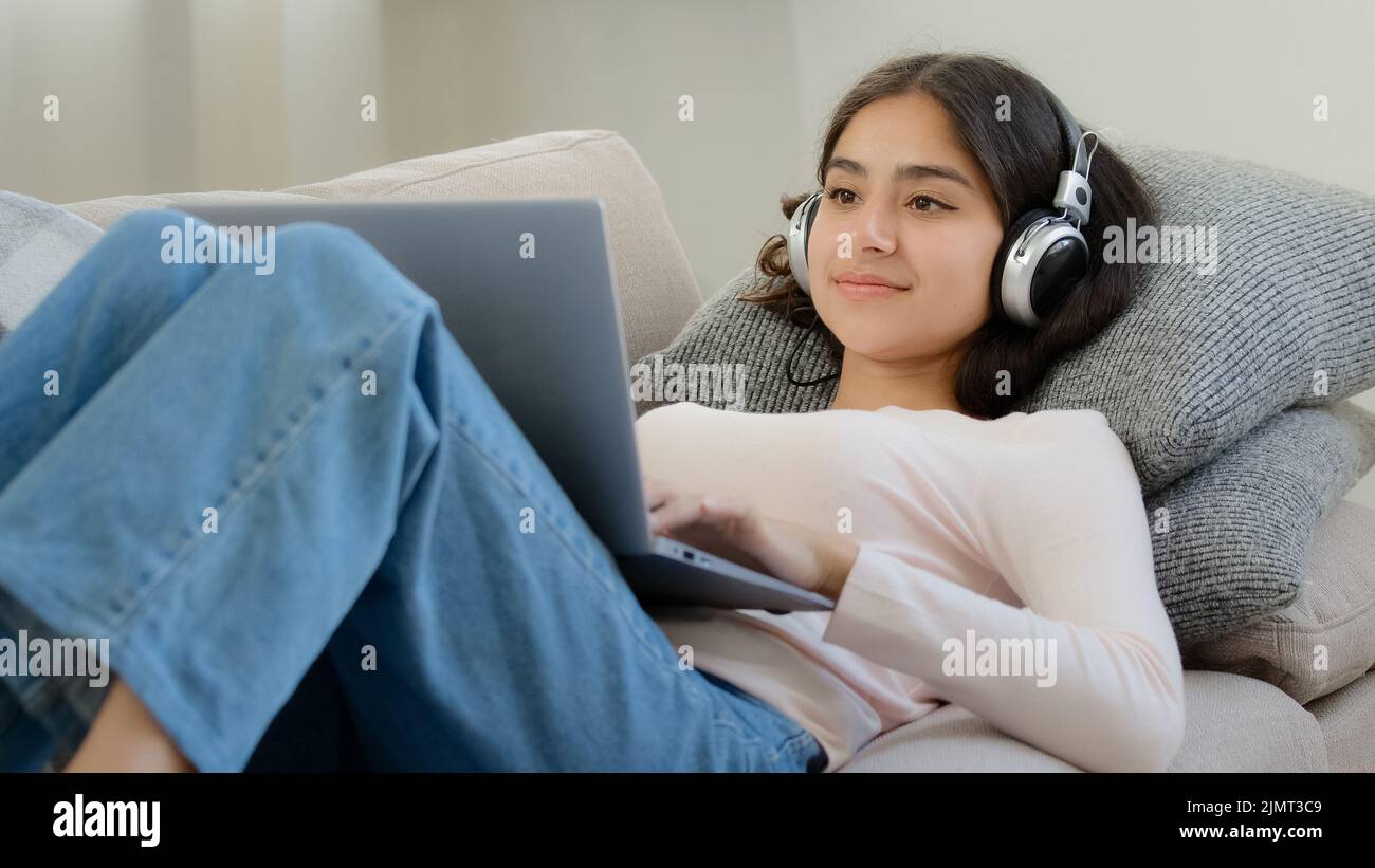 Décontracté arabian woman freelance étudiante réseau de navigation couché sur le canapé regarde l'écran d'ordinateur portable chat jouant en ligne jeu écouter salon Banque D'Images