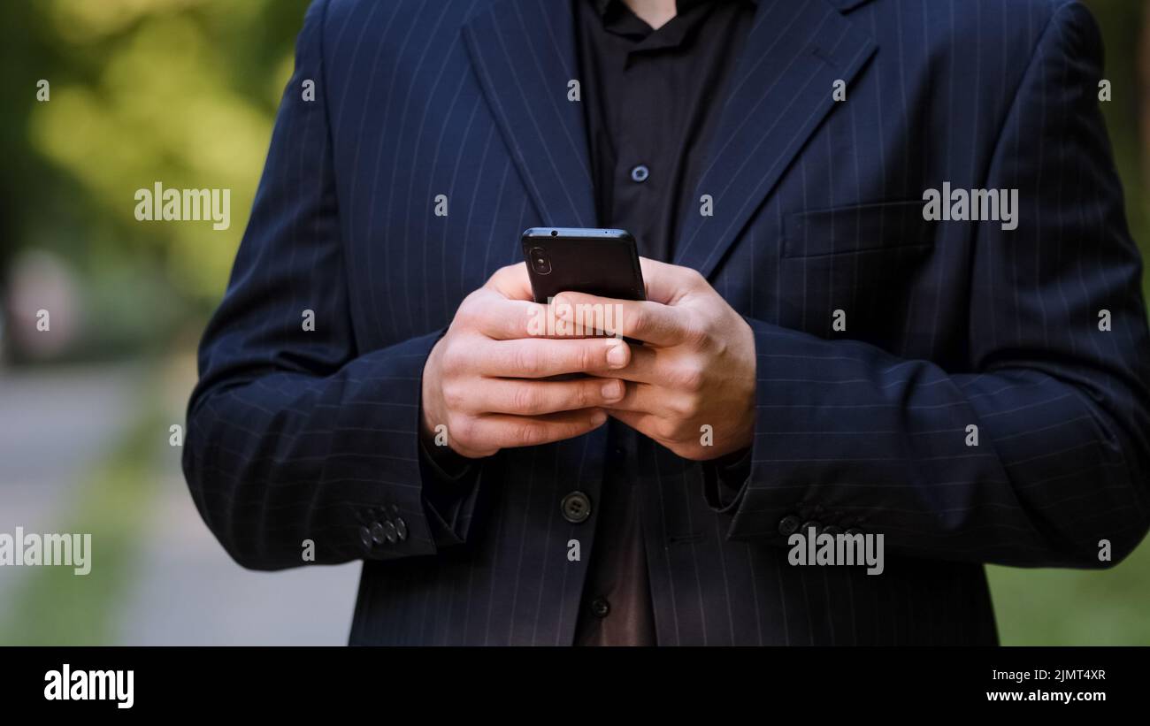 Gros plan hommes mains inconnu homme en noir costume formel tenir smartphone discuter dans les médias sociaux utiliser l'application mobile chat SMS recherche de messages Banque D'Images