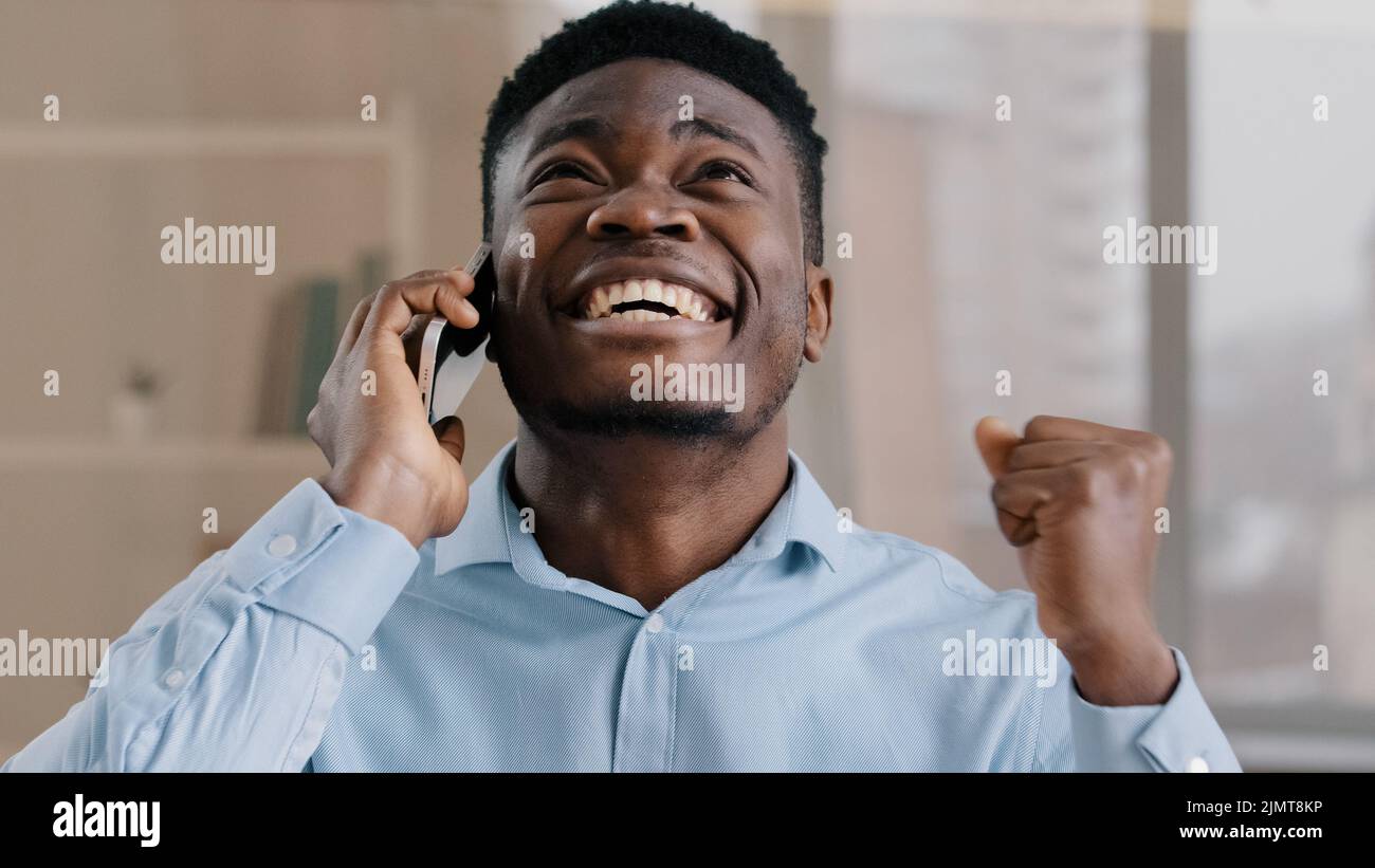 Homme d'affaires afro-américain professionnel homme analyste homme répondre à l'appel entrant parler au téléphone dans le bureau à domicile heureux choqué surpris jeune gars obtenir Banque D'Images