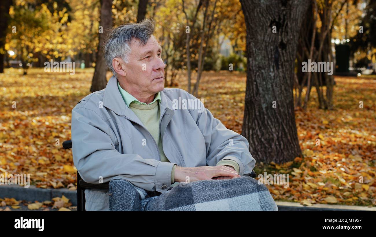 Mature outdoor bouleversé senior retraité caucasien homme grand-père avec une incapacité s'asseoir seul à fauteuil roulant déprimé pensif vieux homme dans plus âgé Banque D'Images