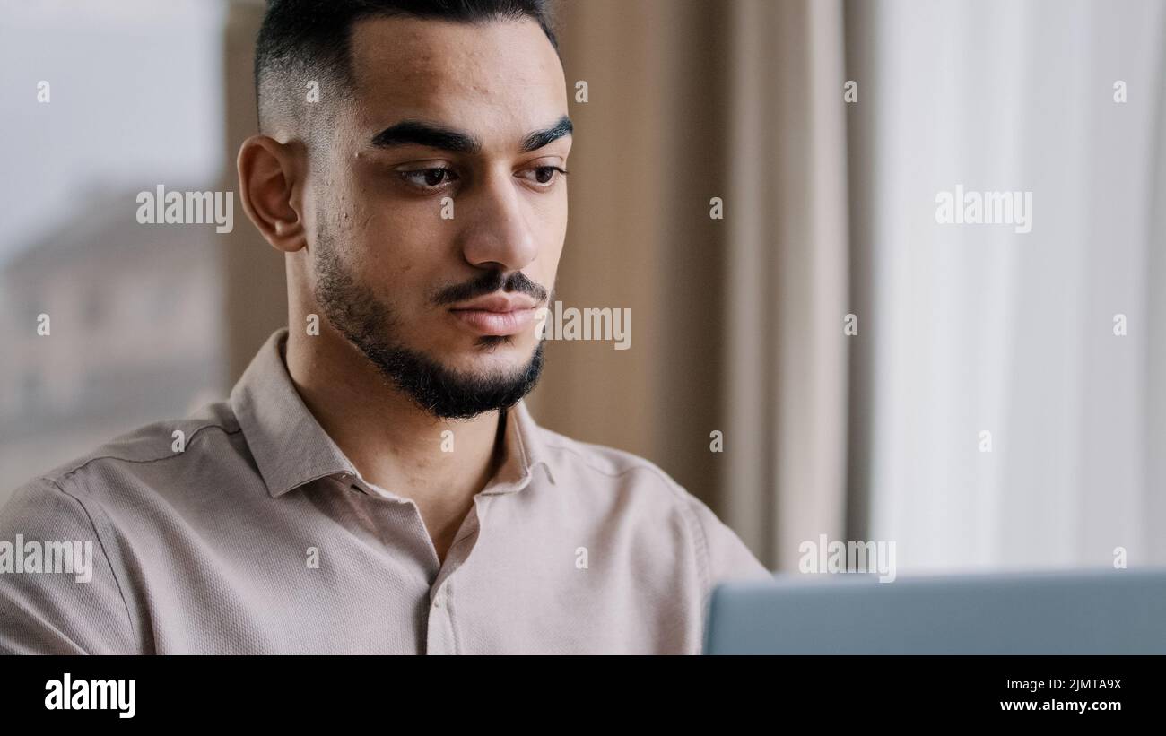 Gros plan sérieux portrait masculin concentré homme d'affaires arabe gars hispanique homme indépendant assis à domicile bureau texting e-mail sur l'utilisation d'ordinateur portable personnel Banque D'Images