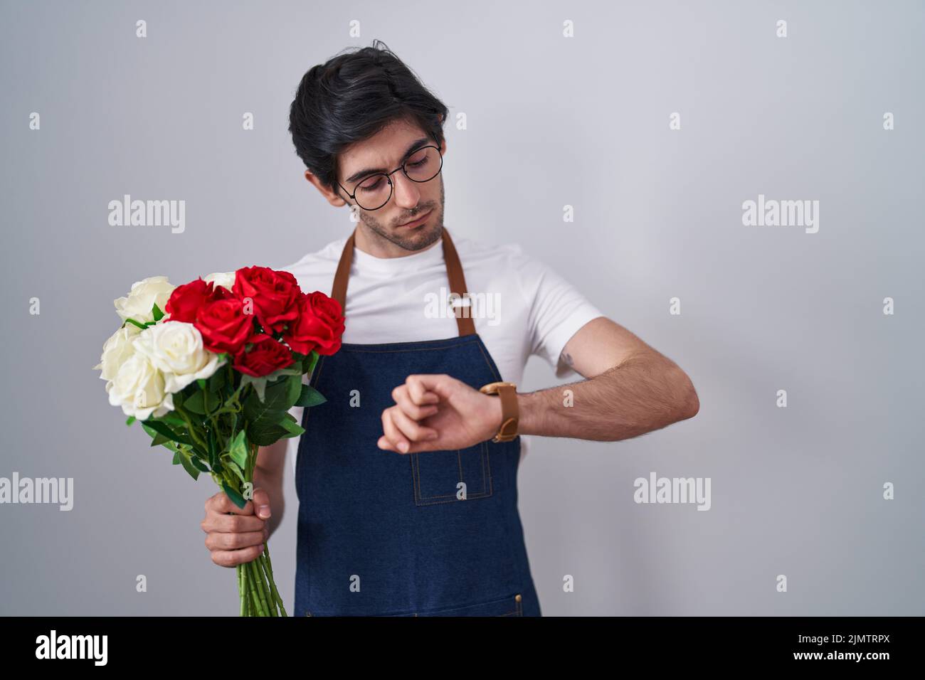 Jeune homme hispanique tenant un bouquet de roses blanches et rouges vérifiant le temps sur la montre de poignet, détendu et confiant Banque D'Images