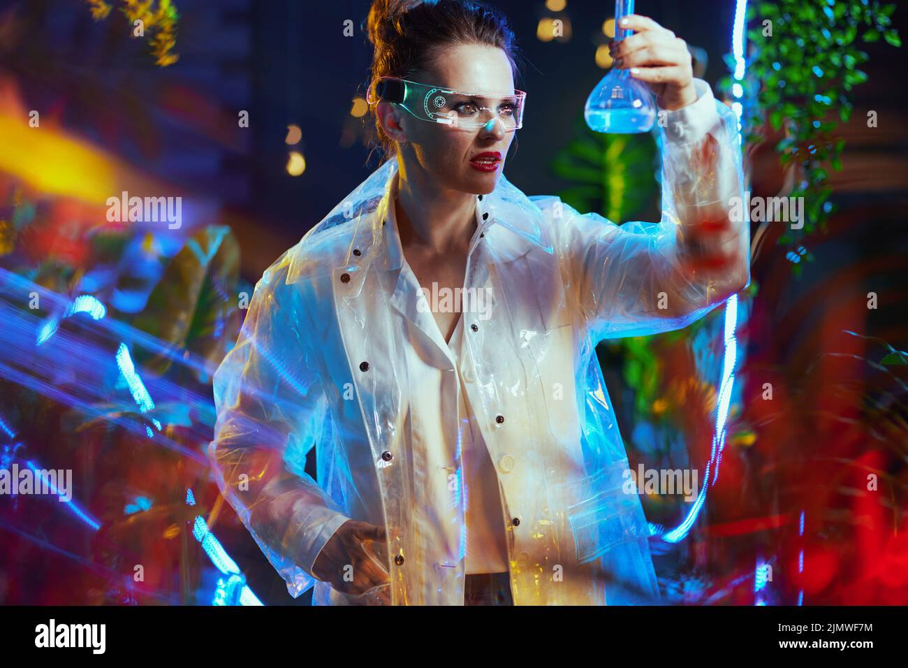 femme scientifique moderne en blouse de laboratoire avec flacon et lunettes futuristes en métaverse. Banque D'Images